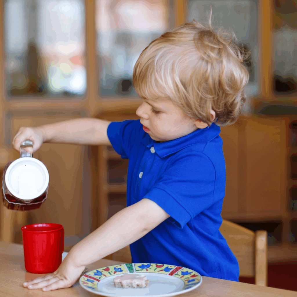 A two year old pouring water from a jug into a cup carefully