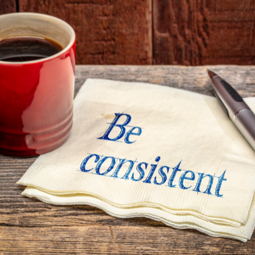 A mug on a table and a napkin with be consistent written on it