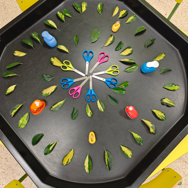 A tough tray table top activity laid out with leaves and scissors to encourage cutting skills and fine motor grip.