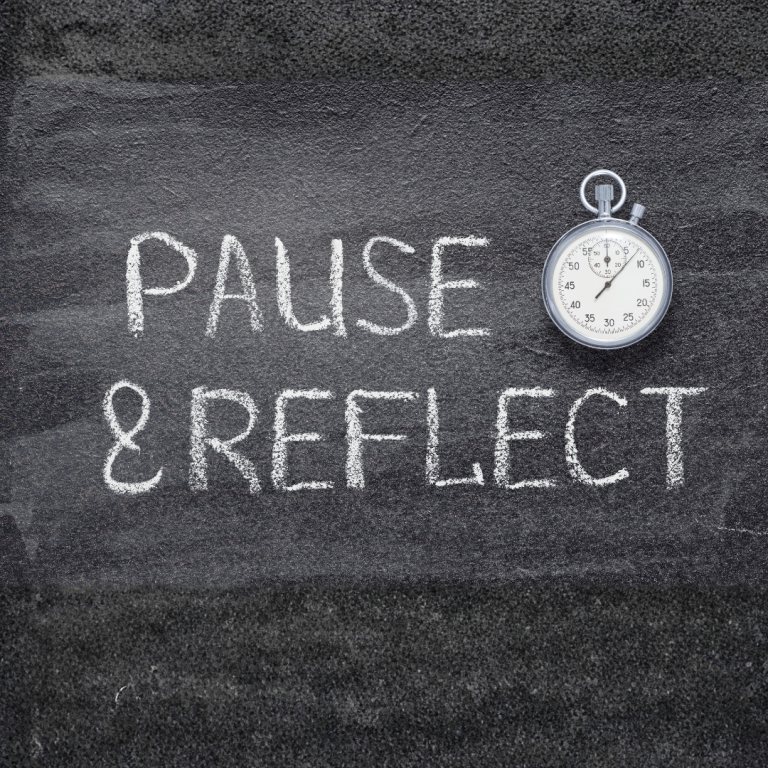 An image of a blackboard with the words Pause and reflect chalked on it