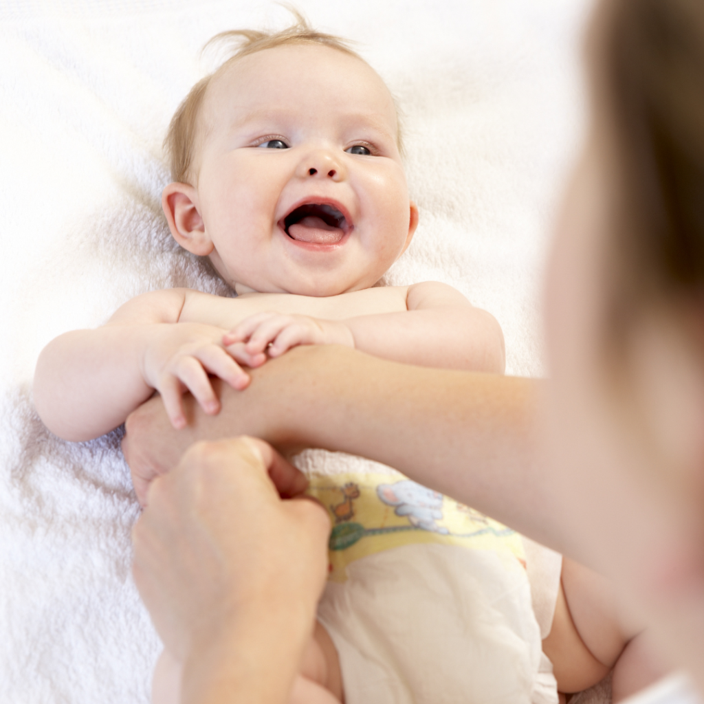 An image of a baby have its nappy changed as the adult talks to it and the baby smiles and learns language