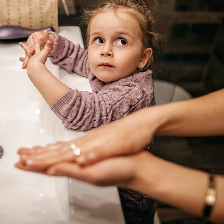 A preschooler washing their hands as an adult models the language