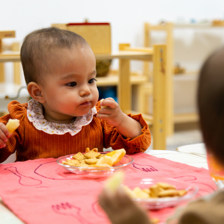 An image of 2 preschoolers sitting at a snack table eating fruit and snacks together