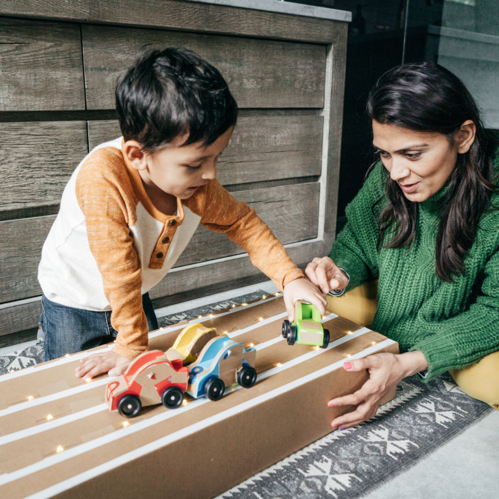 An image of a preschooler and a practitioner engaged in sustained shared thinking and exploring cars and ramps in an early years setting