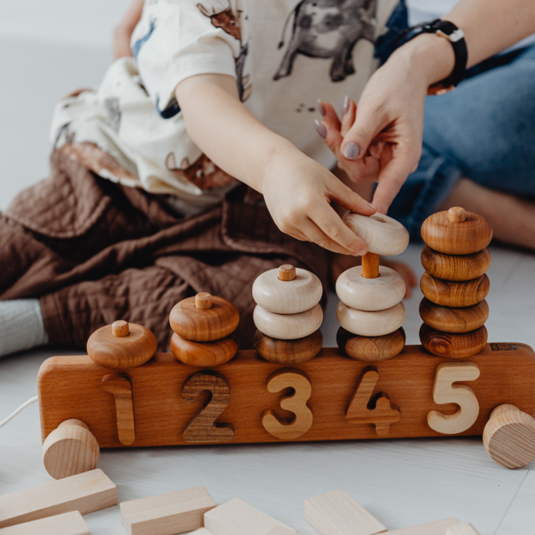 An image of a toddler and an adult engaged in sustained shared thinking whilst solving a block toy puzzle slowly and carefully