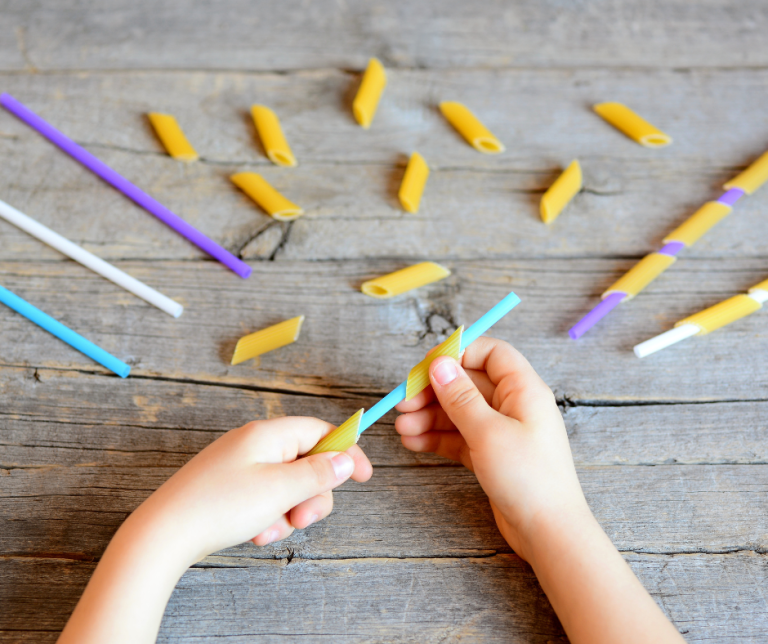 A child putting pasta tubes onto straws