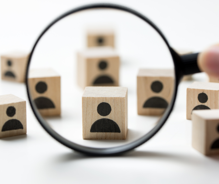 A graphic of a magnifying glass and small wooden pieces representing people