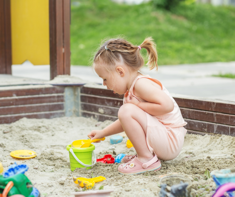 A child playing in a sand pit with containers